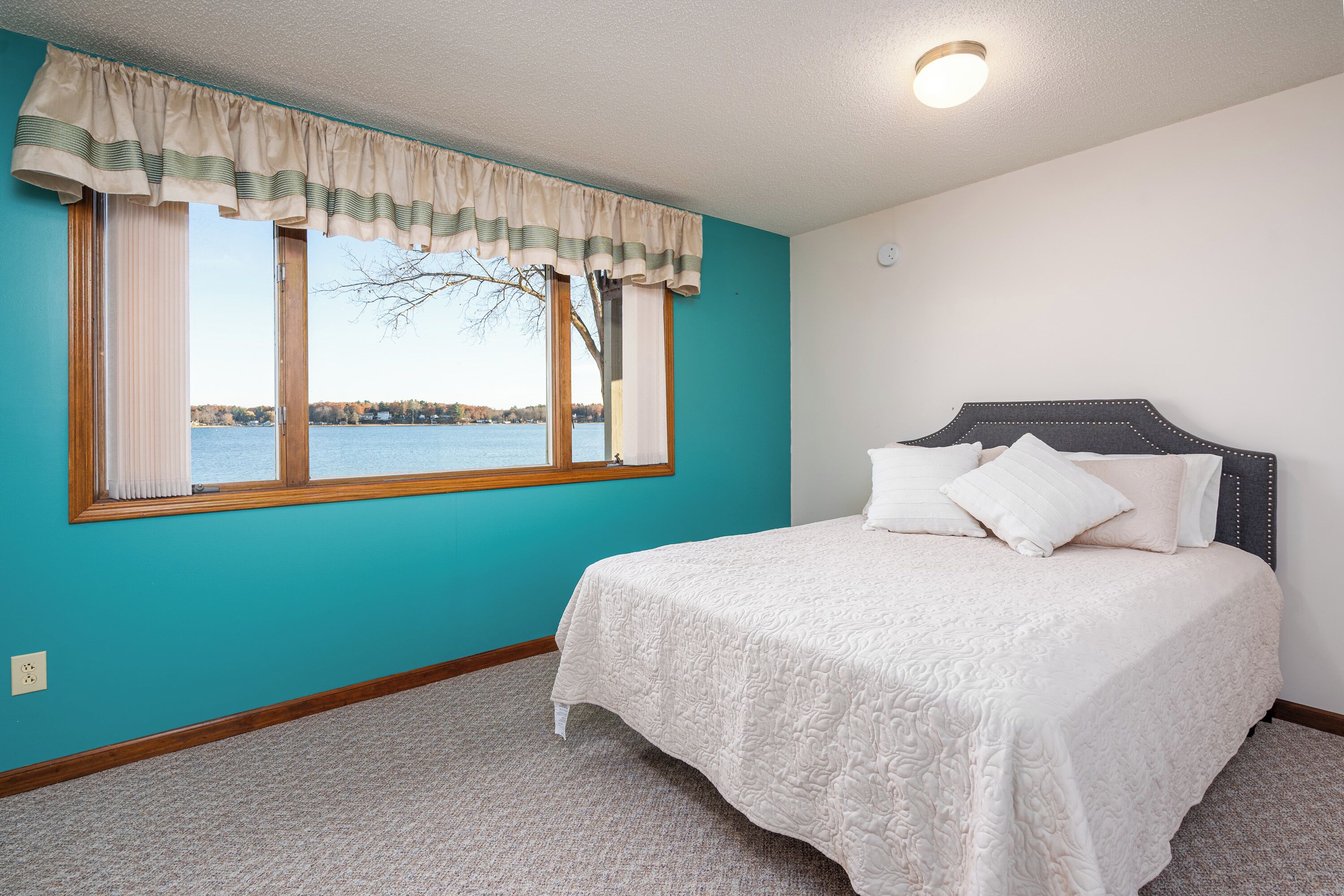 Une chambre avec un grand lit, une fenêtre avec des rideaux et une vue sur un lac.