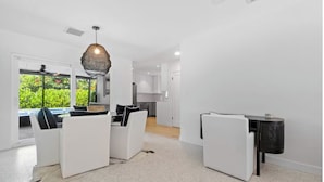 Un salon moderne avec des meubles blancs, une grande fenêtre donnant sur un paysage verdoyant et un luminaire au plafond au design original et à la texture particulière.