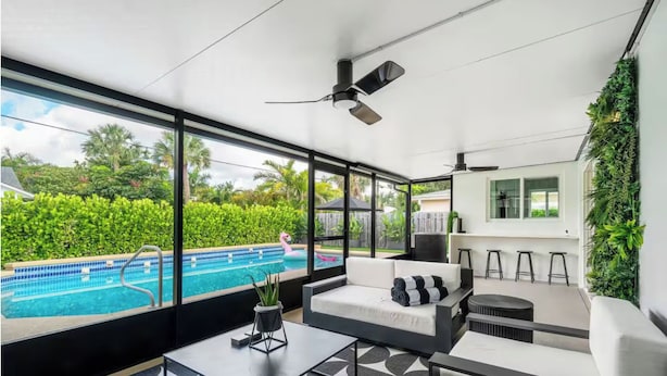 Un espace de détente extérieur moderne, doté d’une piscine, de grandes fenêtres et d’un ventilateur de plafond.