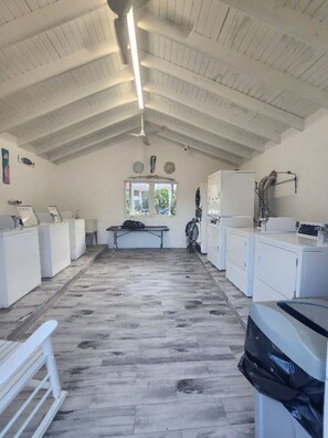 A laundry facility with white washing machines, a drying rack, and a ceiling fan.