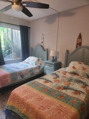 A bedroom with two beds, a ceiling fan, a window with curtains, and a wall decoration.