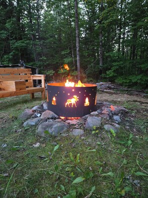 Un feu de camp avec un foyer métallique décoratif, entouré de rochers et d’herbe.