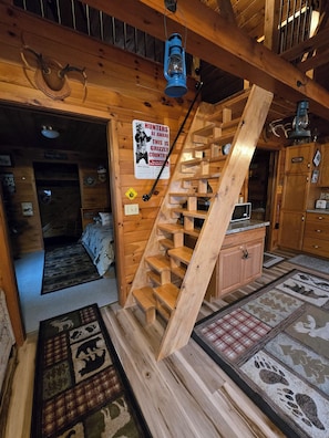 Un intérieur en bois avec un escalier en colimaçon, un lit, un coin cuisine et un panneau d’avertissement concernant la présence d’ours bruns.