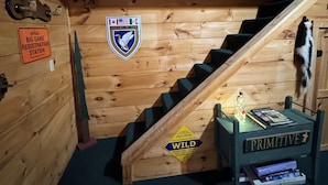 Een houten interieur met een trap, borden met 'The Old Moose Lodge' en 'HIKE', en een bord van 'DUCKS UNLIMITED'.