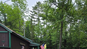 A rustic cabin with a porch, an American flag, and a wooden bench.