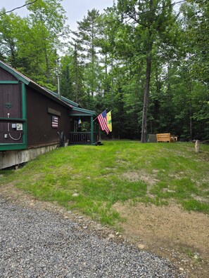 Une cabane rustique dotée d’un porche, d’un drapeau américain et d’un banc en bois.
