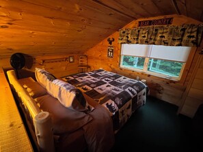 Una habitación acogedora tipo cabaña con techo de madera, una cama con colcha de estampados de animales, un ventanal con vistas a la vegetación y un letrero que dice 'Bear Country'.