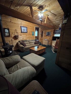 Interior acolhedor de uma cabana de madeira, com um sofá, um banquinho, mesa de centro de madeira e lareira.