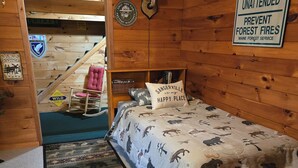 A log cabin room with a bed, a welcome sign, a wildlife sign, and a fire prevention sign.
