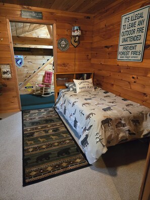 Une chambre aménagée dans un chalet en rondins, avec un lit, un panneau d’accueil, un panneau d’information sur la faune et un panneau de prévention des incendies.
