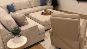 A modern living room with a beige sectional sofa, a round coffee table, and a beige armchair. - Luxury World Cup Escape–Beautiful home w/Pool & Hot Tub - 9 miles from Gillette! (Mansfield)