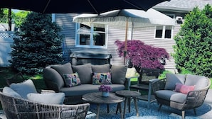 An outdoor seating area with a sofa, chairs, and a table under a large umbrella. - Luxury World Cup Escape–Beautiful home w/Pool & Hot Tub - 9 miles from Gillette! (Mansfield)