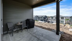 Un patio esterno con un barbecue, due sedie e un tavolino.
