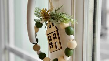 A wooden house ornament with a string of beads and greenery, hanging on a white door.