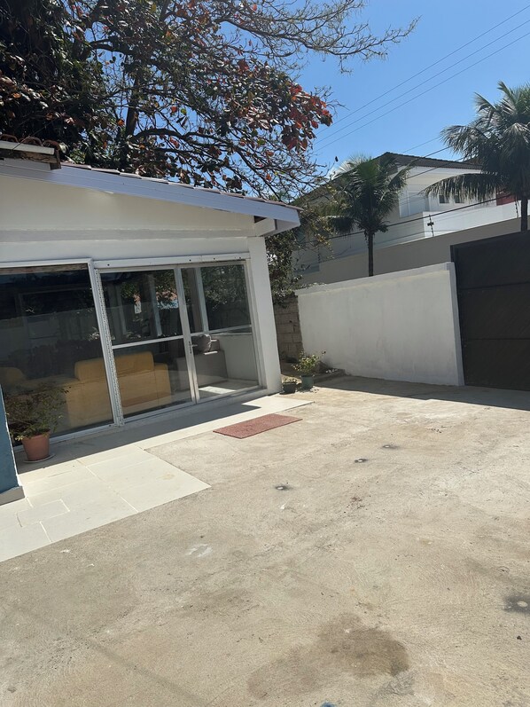 A small, single-story building with a glass door and windows, a concrete patio, and a potted plant. - House in Guarujá with a pool, 200 meters from Pernambuco Beach. (Guarujá)
