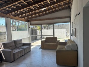 A spacious living area with a high ceiling, large windows, and a view of the outside. - House in Guarujá with a pool, 200 meters from Pernambuco Beach. (Guarujá)