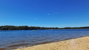 A beach with clear blue water, a sandy shore, and a forested area in the background. - Pool & Beach Access! 'Lake Arrowhead Hideaway' (Nekoosa)