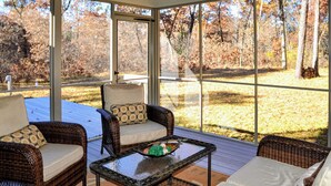 A covered patio with wicker furniture, a glass table, and a view of a wooded area. - Pool & Beach Access! 'Lake Arrowhead Hideaway' (Nekoosa)