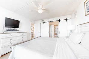 A hotel room with a bed, a TV, a dresser, and a sliding door leading to a bathroom. - 2BR w/ Gulf-View Balcony: Suntide III - Unit 307 (South Padre Island)
