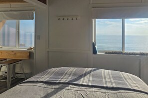 A bedroom with a bed, a desk, and a view of the sea.