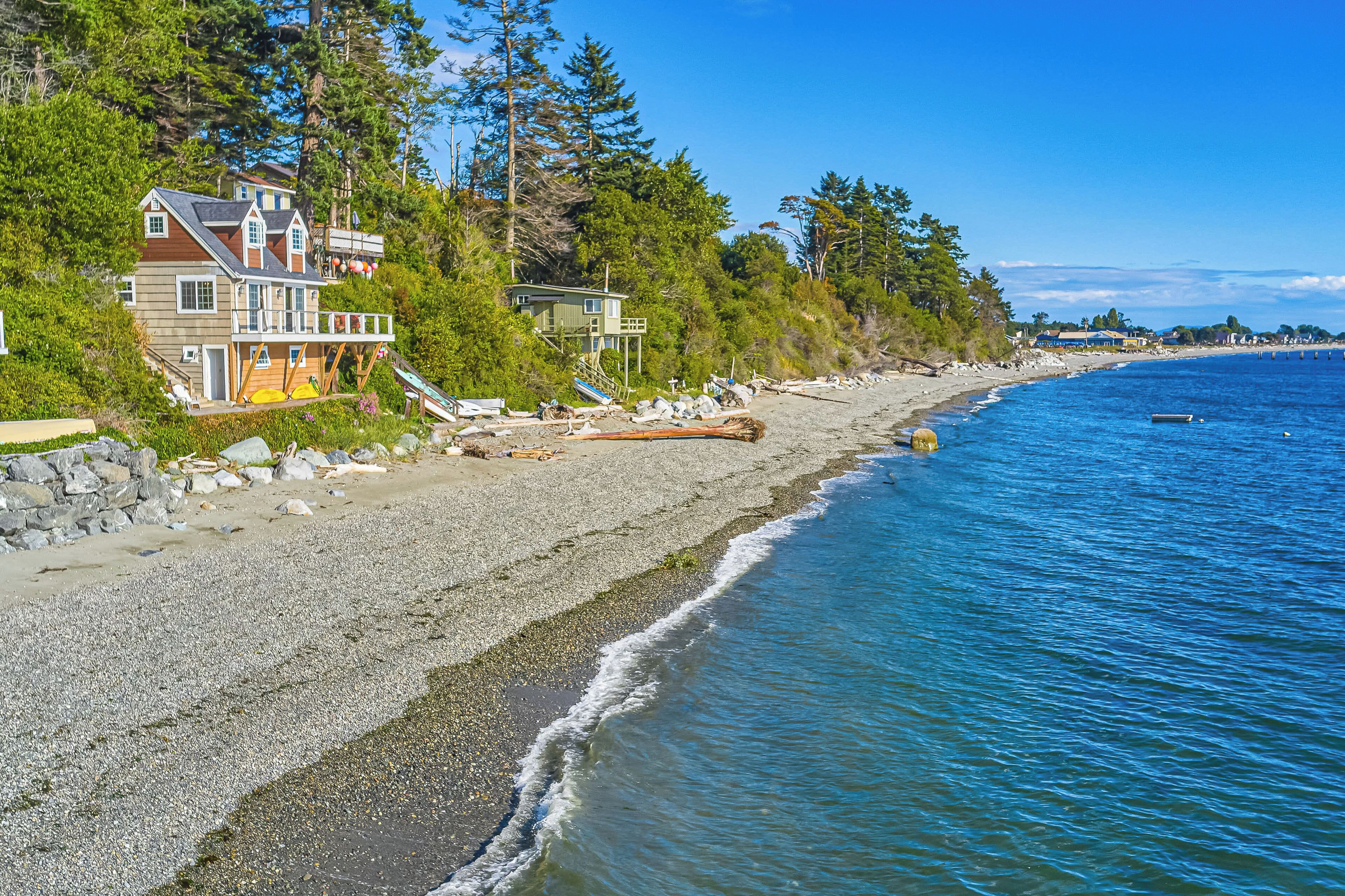 A coastal property with a large house, a wooden deck, and a rocky beach.