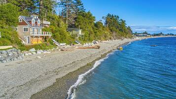 A coastal property with a large house, a wooden deck, and a rocky beach.