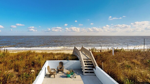 Eine Holzterrasse mit einer Treppe, die zum Strand führt.