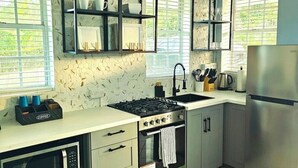 Cocina moderna con estufa a gas, horno, microondas y refrigerador de acero inoxidable. Cuenta con alacenas y un salpicadero con diseño de panal, además de una ventana con persianas.