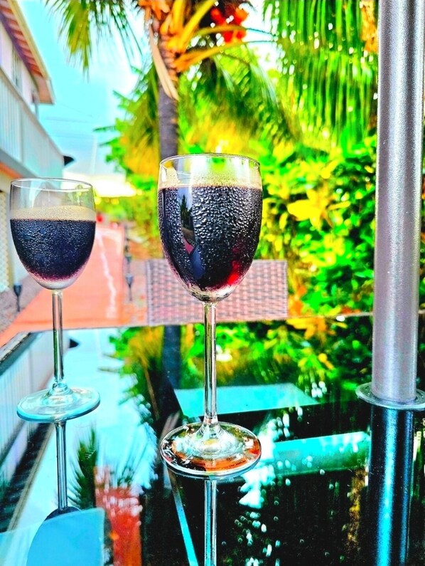 Two wine glasses on a balcony with a view of greenery and a building in the background.