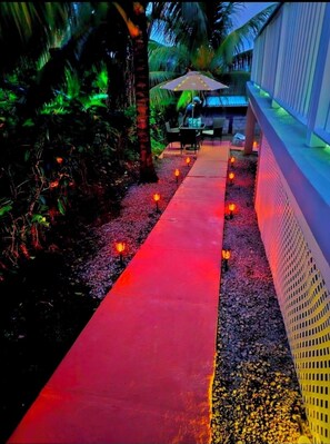 A pathway with red lighting, palm trees, and outdoor seating.