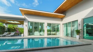 Un espace moderne aménagé au bord de la piscine, avec une piscine à eau claire, des chaises longues et un coin salon abrité.