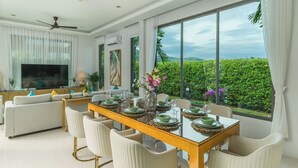 Une salle à manger moderne avec une grande table dressée pour six personnes, un canapé et un téléviseur en arrière-plan.