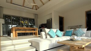A modern living room with a sofa, coffee table, and a dining area with a bench and table. - Luxury 3BR Pool Villa near Blue Tree - Bang Tao (Si Sunthon)