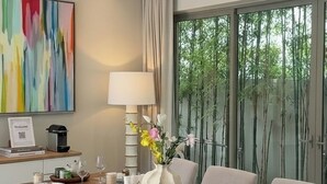 A modern dining room with a wooden table, cushioned benches, and a large window with a view of bamboo trees. - Luxury 3BR Pool Villa near Blue Tree - Bang Tao (Si Sunthon)