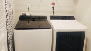 A laundry room with two dryers, a power outlet, and a shelf with a box.