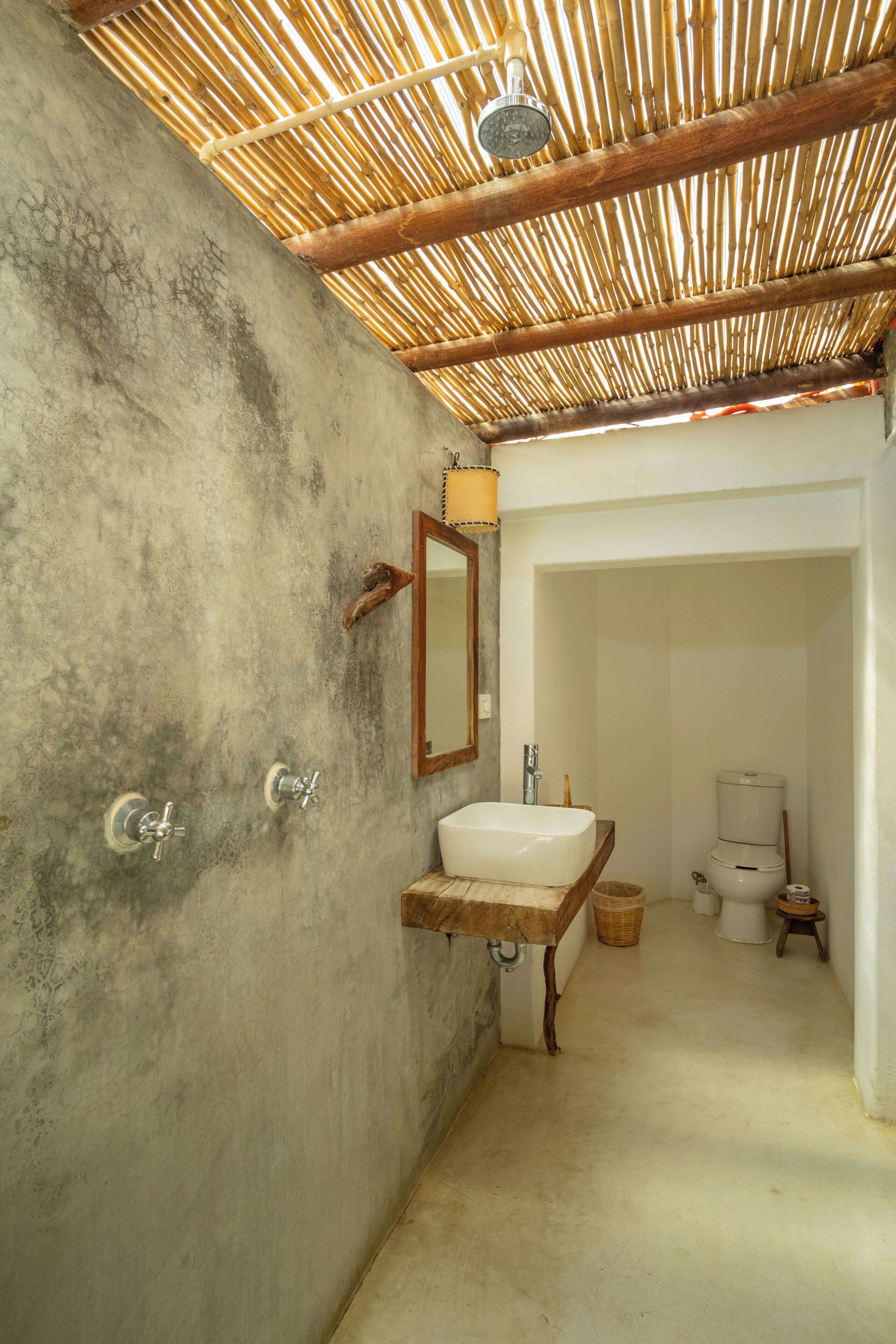 A bathroom with a concrete wall, a wooden ceiling, a wooden sink, a mirror, a shower, and a toilet.