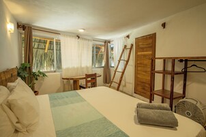 Un dormitorio con cama, escritorio, silla, escalera, ventilador y ventana con cortinas.