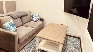 A living room with a beige sofa, patterned cushions, a wooden coffee table, a patterned rug, and a flat-screen TV mounted on the wall. - Tiny Mansion in Naples. 5 mins to Beach (Naples)