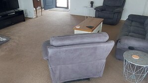 A living room with a grey sofa, a coffee table, and a grey armchair. There is a TV on the left and a door leading outside. - Located 5 mins drive from the town.  Pets are not allowed. (Te Awamutu)