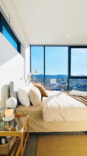 A modern bedroom with a large bed, a bedside table with a lamp, and a view of a cityscape through large windows. - Amazing Views - 2BD 2BA Homey Toowong Abode + Pool (Toowong)