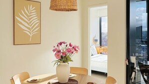A dining area with a round wooden table, six chairs, a woven pendant light, a vase with pink flowers, and a framed leaf artwork on the wall. - Amazing Views - 2BD 2BA Homey Toowong Abode + Pool (Toowong)