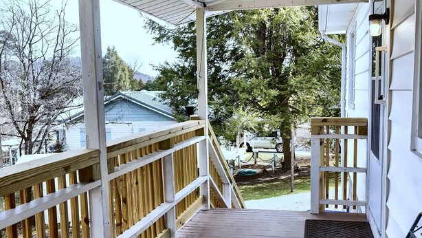 A covered porch with a wooden railing, a bench, and a view of a house and trees. - Cozy 2-bedroom home in Oak Ridge - 1940s themed (Oak Ridge)