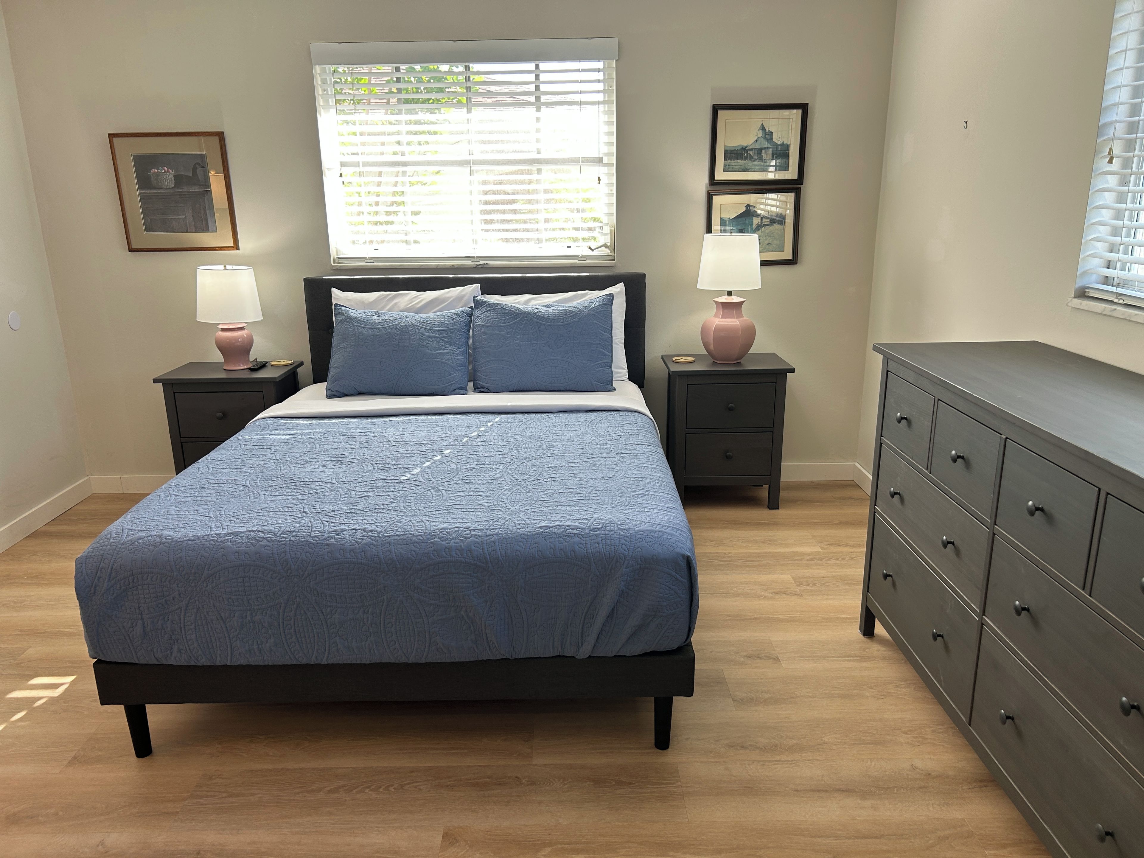 A bedroom with a bed, two bedside tables with lamps, a dresser, and framed pictures on the wall.
