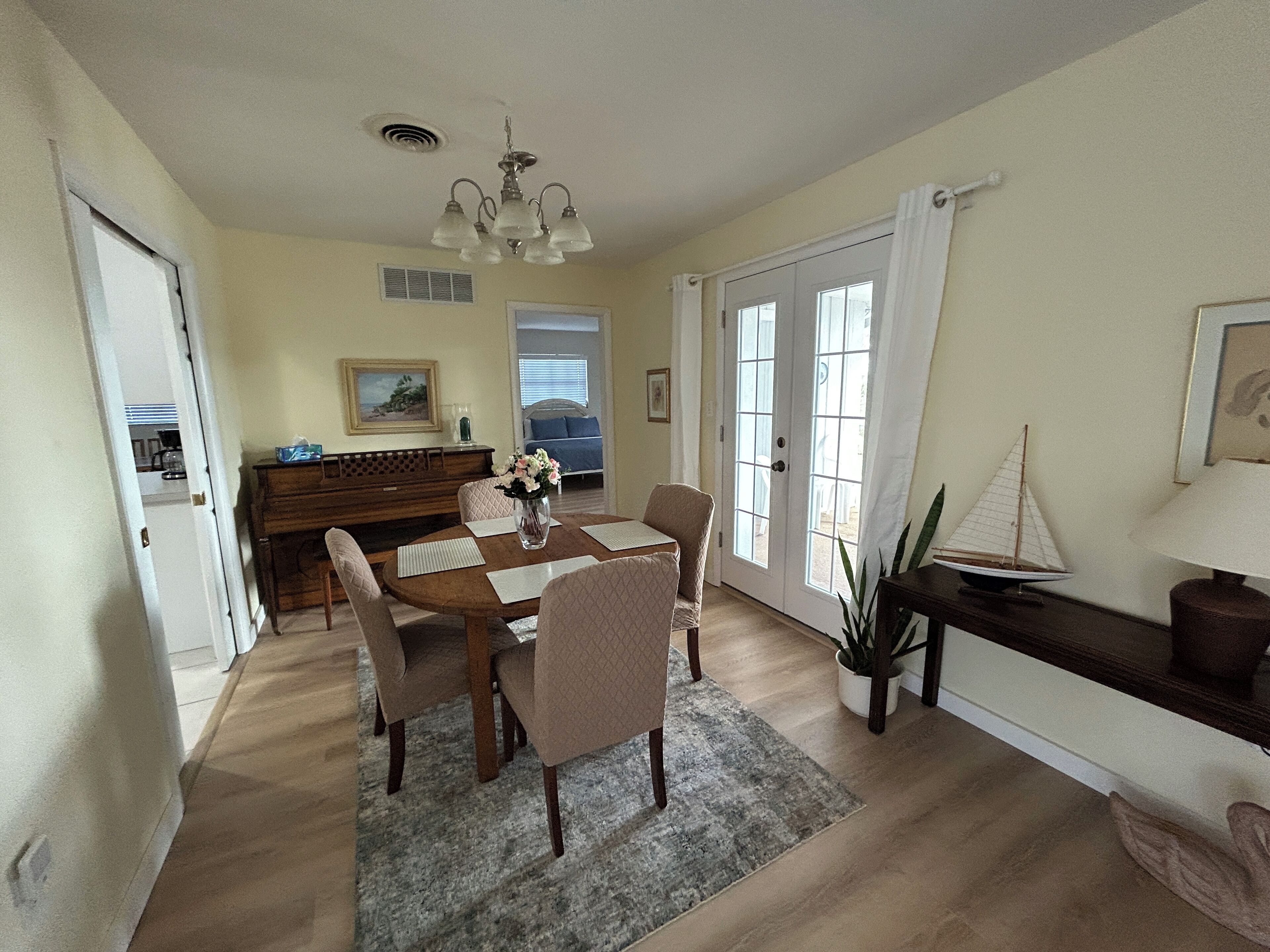 A dining area with a wooden table, four chairs, a vase with flowers, a ceiling fan, and a view through a glass door.