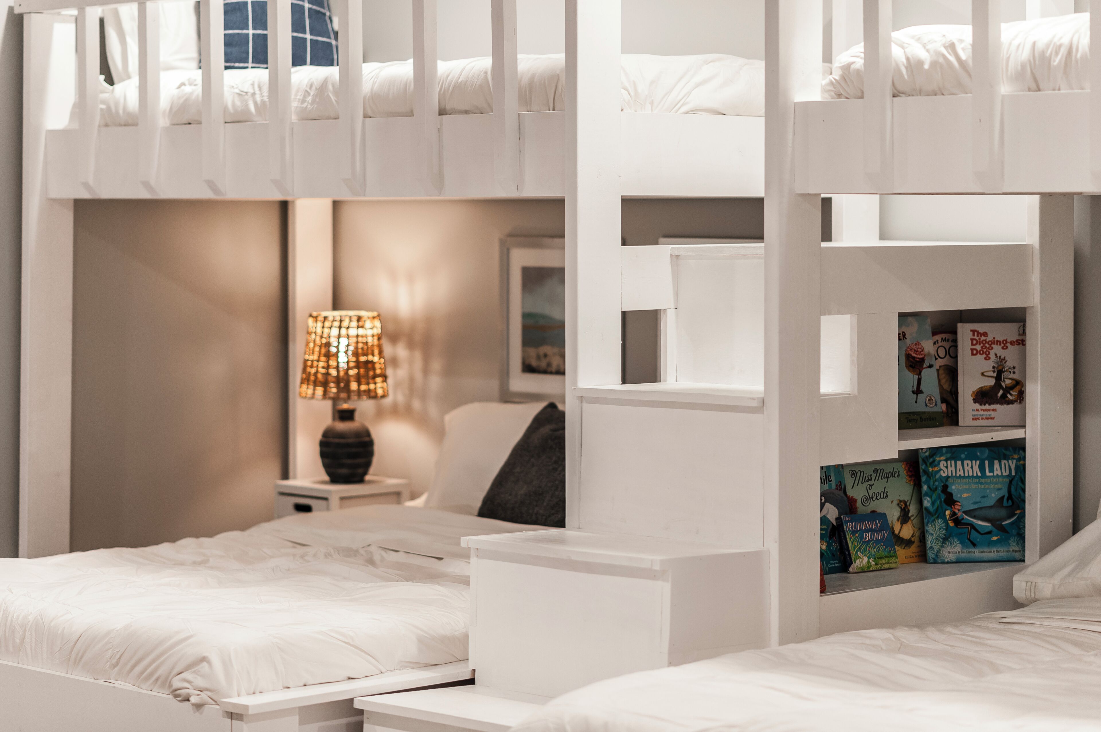A bunk bed room with a bedside table, a lamp, and bookshelves.
