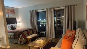 Hotelkamer met een bed, een bank, een bijzettafeltje en uitzicht op de stad 's nachts.
