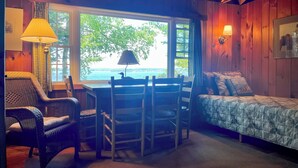 A cozy room with a wooden ceiling, a large window with a view of the outdoors, a bed with a quilt, a desk with chairs, and a lamp. - Bay-View Getaway w/ Deck Between Camden & Belfast! (Northport)