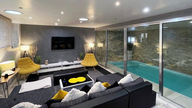 Un salon moderne avec un canapé noir, des fauteuils jaunes, une table basse et un téléviseur fixé au mur.