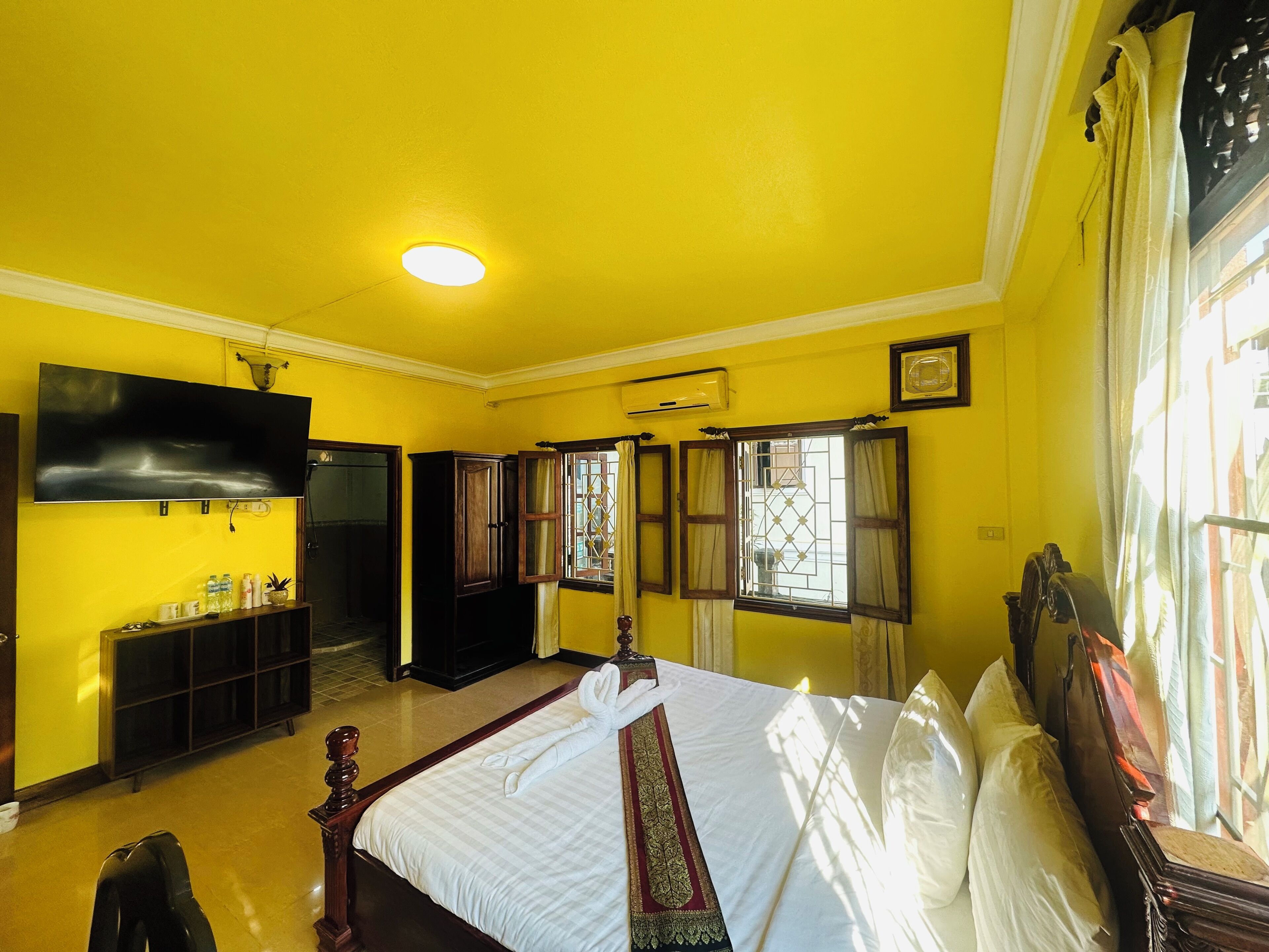 Habitación de hotel con cama, televisor, armario y ventana con cortinas.
