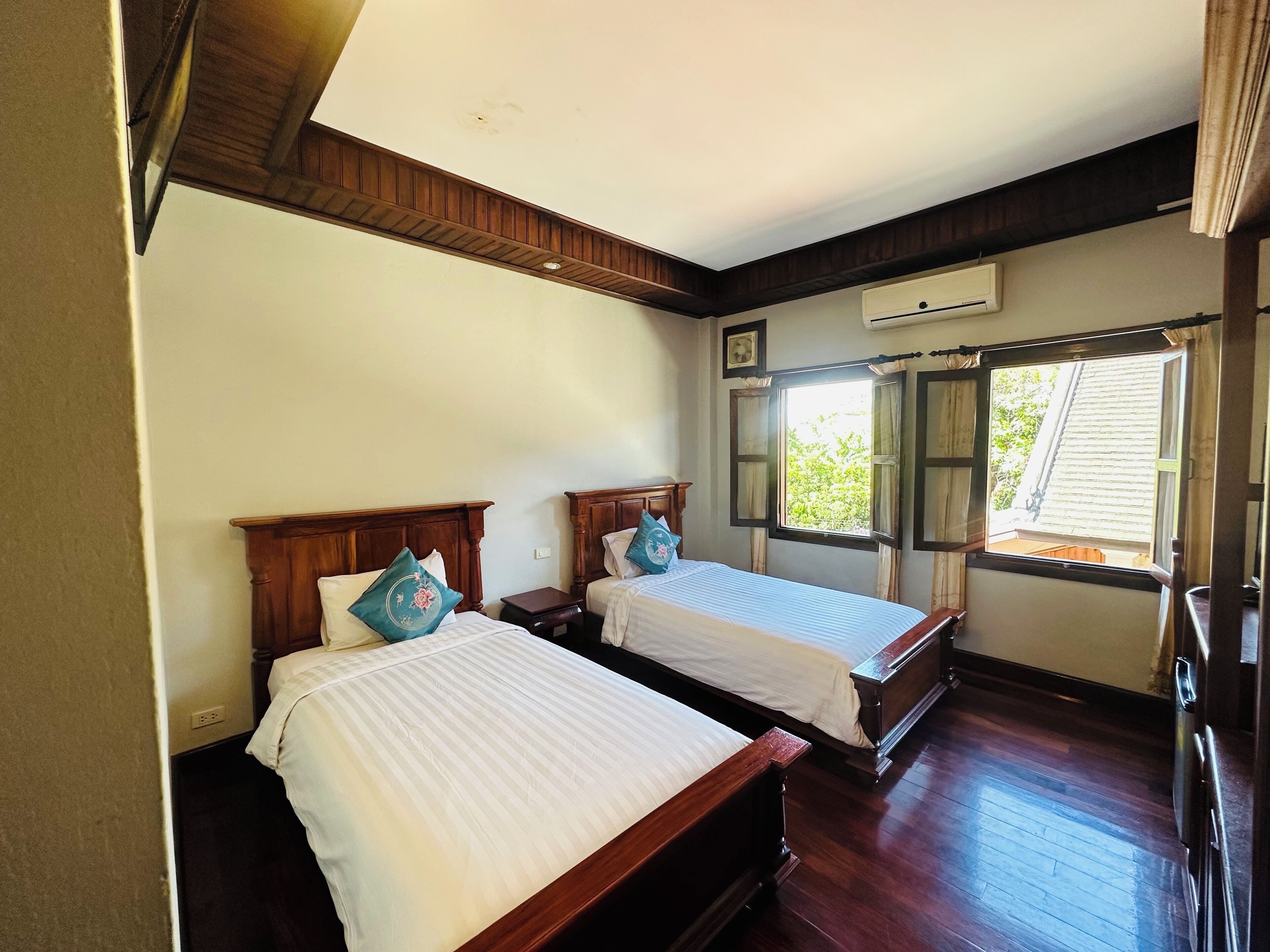 Une chambre avec deux lits en bois, une fenêtre avec des rideaux et un appareil de climatisation fixé au mur.